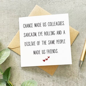 May include: A white card with black text that reads "Chance made us colleagues. Sarcasm, eye rolling and a dislike of the same people made us friends." There are three small red hearts at the bottom of the card.