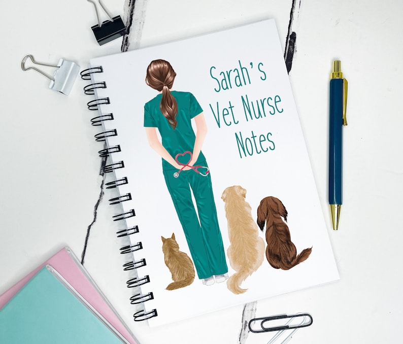 K&ouml;nnte beinhalten: Ein wei&szlig;es Notizbuch mit Spiralbindung und einer gr&uuml;nen und braunen Illustration einer Tierarzthelferin mit Stethoskop und drei Hunden. Der Text auf dem Cover lautet "Sarah's Vet Nurse Notes".