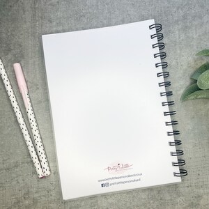May include: A white spiral bound notebook with a blank cover. The notebook has a black wire binding and a small logo on the back cover that says "Pretty Little" with a website address and social media handles.