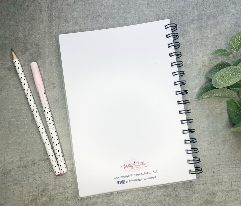 May include: A white spiral bound notebook with a blank cover. The notebook has a black wire binding and a small logo on the back cover that says "Pretty Little" with a website address and social media handles.