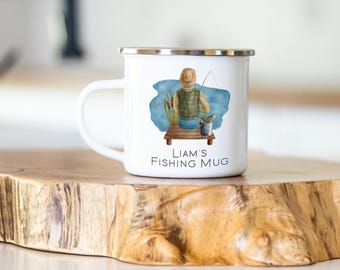 May include: A white enamel mug with a silver rim featuring a watercolor illustration of a person fishing from a wooden dock. The design includes a blue water background, cattails, and a bucket. The text reads LIAM'S FISHING MUG.