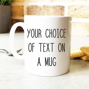以下が含まれることがあります： 白いセラミック製のマグカップに、黒い文字で「YOUR CHOICE OF TEXT ON A MUG」と書いてあります。