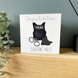 Op de afbeelding: Een witte kaart met een zwart-witte illustratie van een politiekostuum, handboeien en laarzen. De tekst "Congratulations" staat bovenaan de kaart en "Sergeant Hales" onderaan.