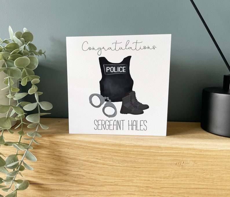 Op de afbeelding: Een witte kaart met een zwart-witte illustratie van een politiekostuum, handboeien en laarzen. De tekst "Congratulations" staat bovenaan de kaart en "Sergeant Hales" onderaan.