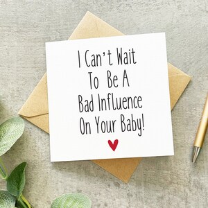 May include: A white card with black text that reads "I Can't Wait To Be A Bad Influence On Your Baby!" with a red heart at the bottom.