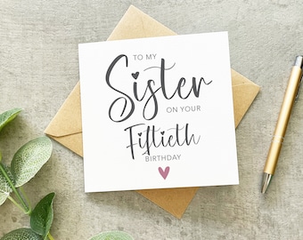 May include: A white card with the text "To my Sister on your Fiftieth Birthday" in black script. A small pink heart is below the text.
