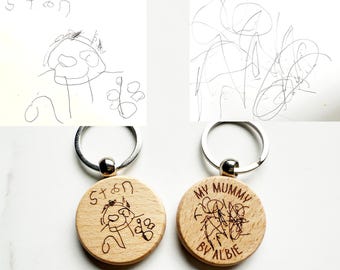 May include: Two wooden keychains with silver rings. One keychain features a child's drawing and the name "Stan". The other keychain has a drawing and the text "MY MUMMY BY ALBIE". Both keychains are round.