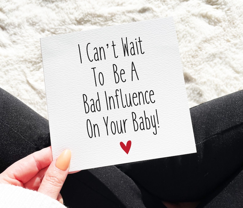 May include: A white card with black text that reads "I Can't Wait To Be A Bad Influence On Your Baby!" with a red heart at the bottom.