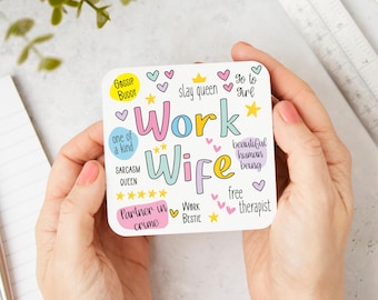 May include: A white card with pink, blue and yellow text that reads "Work Wife". The card is decorated with hearts, stars and crowns. The text on the card includes phrases like "Gossip Buddy", "Slay Queen", "One of a Kind", "Sarcasm Queen", "Partner in Crime", "Work Bestie", "Go to Girl", "Beautiful Human Being", "Free Therapist".