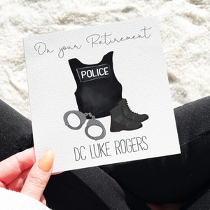 May include: A white card with black text that reads "On your Retirement" and a black and white illustration of a police officer's uniform, handcuffs, and boots. The text "DC LUKE ROGERS" is printed below the illustration.