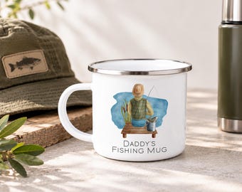 May include: A white enamel mug with a silver rim featuring a watercolor illustration of a person fishing from a wooden dock. The text DADDY'S FISHING MUG is printed in black below the illustration. The mug has a handle on the left side.