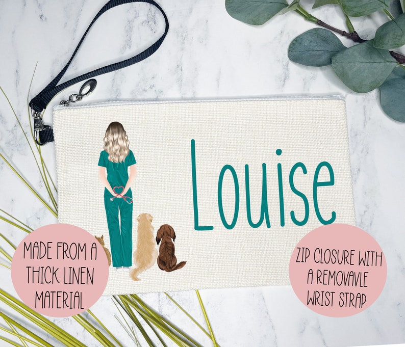 K&ouml;nnte beinhalten: Eine wei&szlig;e Kosmetiktasche aus Canvas mit einem t&uuml;rkisfarbenen Rei&szlig;verschluss und einem t&uuml;rkisfarbenen Handgelenkband. Die Tasche zeigt eine Comic-Illustration einer Frau in Scrubs mit drei Hunden. Der Text "Louise" ist in T&uuml;rkis auf der Tasche aufgedruckt. Die Tasche ist aus dickem Leinenstoff gefertigt.