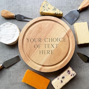 May include: A wooden cheese board with the text "YOUR CHOICE OF TEXT HERE" surrounded by various cheeses and cheese knives. Cheeses include a wedge of blue cheese, a block of cheddar, and a round of brie. The knives have wooden handles.