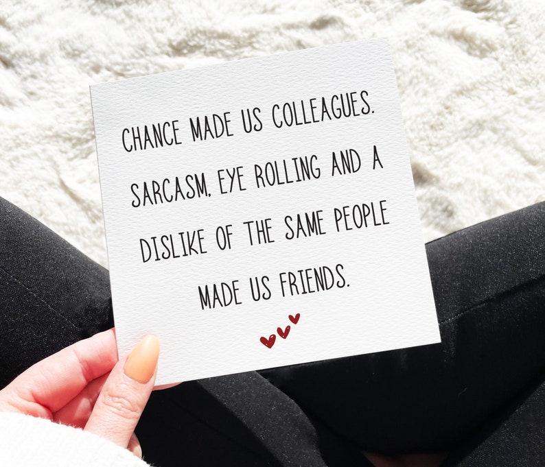 May include: A white card with black text that reads "CHANCE MADE US COLLEAGUES. SARCASM, EYE ROLLING AND A DISLIKE OF THE SAME PEOPLE MADE US FRIENDS." There are three red hearts at the bottom of the card.