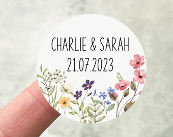 May include: Round white sticker with a floral design. The sticker has the text "CHARLIE & SARAH 21.07.2023" in black.