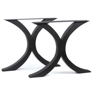 May include: Two black, curved metal table legs. Each leg has a wide, flat top and a curved, arching design that tapers to a flat base. The legs are designed to support a tabletop and have a modern aesthetic.