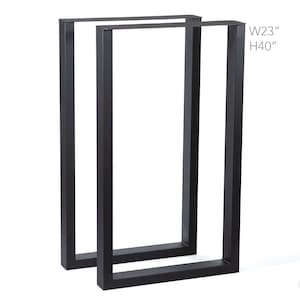 May include: Two black metal table legs. Each leg is rectangular, with a width of 23 inches and a height of 40 inches. The legs are displayed against a white background. Text on the image reads: W23" H40".