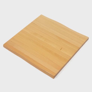 May include: A square, light-colored wooden cutting board. The board is made of multiple strips of wood joined together, creating a striped pattern. The edges are smooth and the overall appearance is clean and simple.