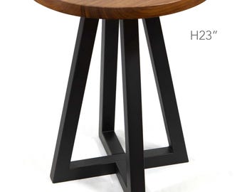 May include: A round side table with a natural brown wood grain top and a black metal base featuring four angled legs connected by a cross-shaped support at the bottom. The text H23" is printed on the right side, indicating a height of 23 inches.