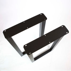 May include: Two black metal table legs, one taller than the other, with a rectangular shape and a flat top. The legs are made of sturdy metal and have a black powder coat finish.