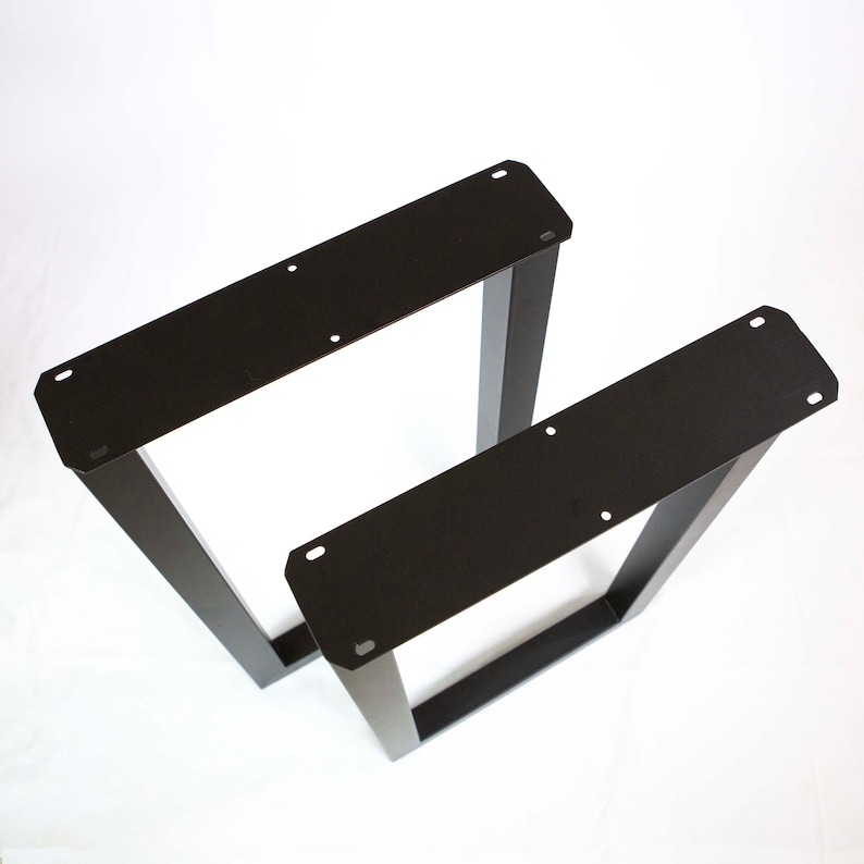 May include: Two black metal table legs, one taller than the other, with a rectangular shape and a flat top. The legs are made of sturdy metal and have a black powder coat finish.