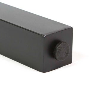 May include: Close-up of a black, rectangular furniture leg with a matte finish. A circular, textured knob is visible on the end. The leg is designed for furniture and has a modern, minimalist aesthetic.