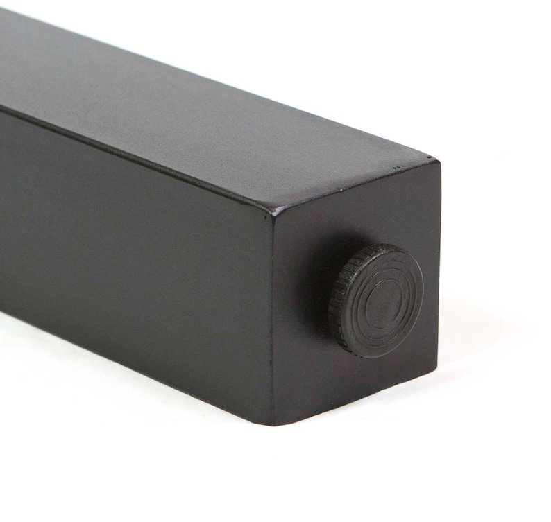May include: Close-up of a black, rectangular furniture leg with a matte finish. A circular, textured knob is visible on the end. The leg is designed for furniture and has a modern, minimalist aesthetic.