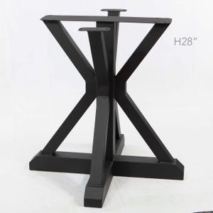 May include: Black metal table base with an X-shaped design. The base has a height of 71 cm. The legs are angled and meet at a central point, creating a sturdy and modern look. The base is suitable for a dining table or coffee table.