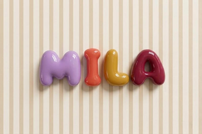 May include: The name MILA spelled out in individual, three-dimensional, glossy, balloon-style letters. The letter M is light purple, the I is coral, the L is mustard yellow, and the A is deep magenta, all arranged horizontally in a row.