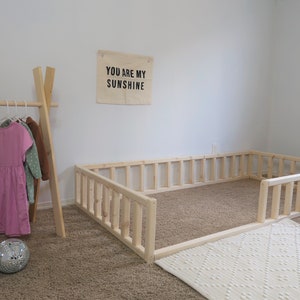 Puede incluir: Un &aacute;rea de juego con marco de madera clara y una alfombra blanca estampada. Un perchero de madera sostiene vestidos en rosa, verde y marr&oacute;n. Dos bolas de discoteca est&aacute;n en el suelo. Una pancarta en la pared dice "YOU ARE MY SUNSHINE".
