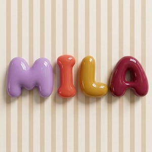 May include: The name "MILA" in glossy, 3D letters. The letters are purple, orange, yellow, and burgundy, against a striped beige and white background. A decorative item.