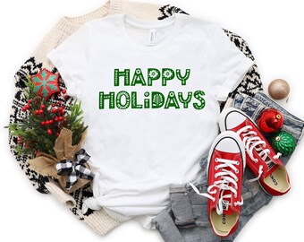 May include: White t-shirt with the text "HAPPY HOLIDAYS" in green letters with a festive design. The letters are outlined in white.