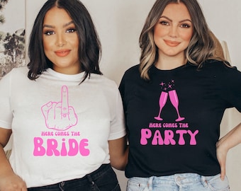 May include: Two women wearing white and black t-shirts with pink text that says "Here comes the bride" and "Here comes the party".