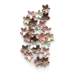 以下が含まれることがあります： ベージュ、ピンク、ブラウンの色合いの小さな紙の花の集まり。花は白い背景に緩やかに集められています。