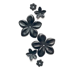 Può includere: Cinque decorazioni floreali in pelle nera di diverse dimensioni. I fiori hanno cinque petali e un piccolo foro al centro.