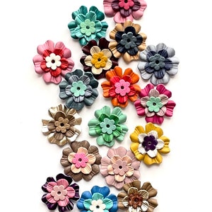 Könnte beinhalten: Sortiment von 18 bunten Lederblumen-Verzierungen. Die Blumen sind in verschiedenen Schattierungen von Rosa, Blau, Grün, Gelb und Braun. Jede Blume hat einen Mittelknopf in einer anderen Farbe.