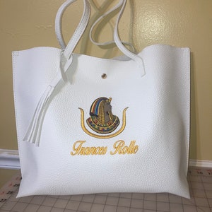 May include: White tote bag with a gold embroidered image of an Egyptian queen and the text "Frances Rolle".