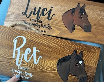 May include: Two wooden signs with painted horse portraits and names. The top sign reads "Luci Lovedby The Lowery Family #445.0287". The bottom sign reads "Ret Lovedby Lauren Day 467.8010".