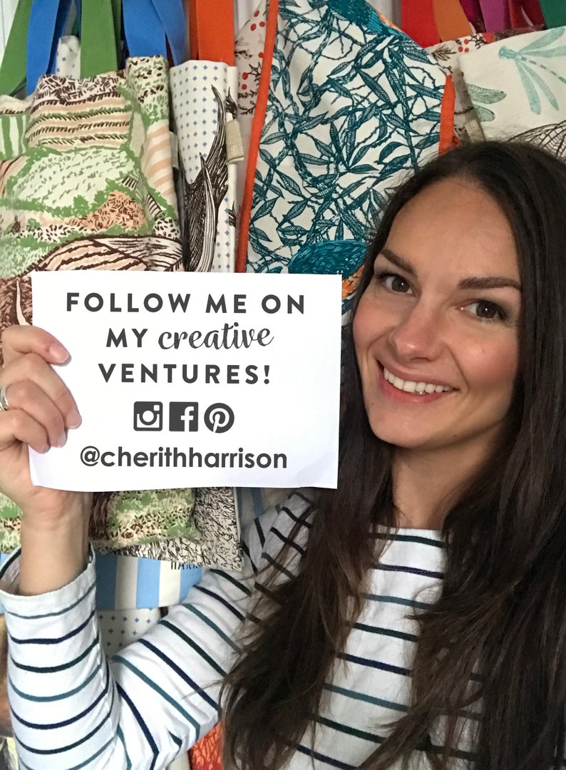 Puede incluir: Una mujer sosteniendo una tarjeta blanca con el texto "FOLLOW ME ON MY CREATIVE VENTURES! @cheriththarrison" y los iconos de redes sociales para Instagram, Facebook y Pinterest. Lleva una camisa a rayas y tiene el pelo largo y casta&ntilde;o.