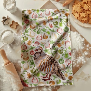 May include: A white kitchen towel with a colorful pear pattern and a detailed illustration of a bird. The towel is surrounded by baking supplies, including flour, cookie cutters, and a rolling pin.