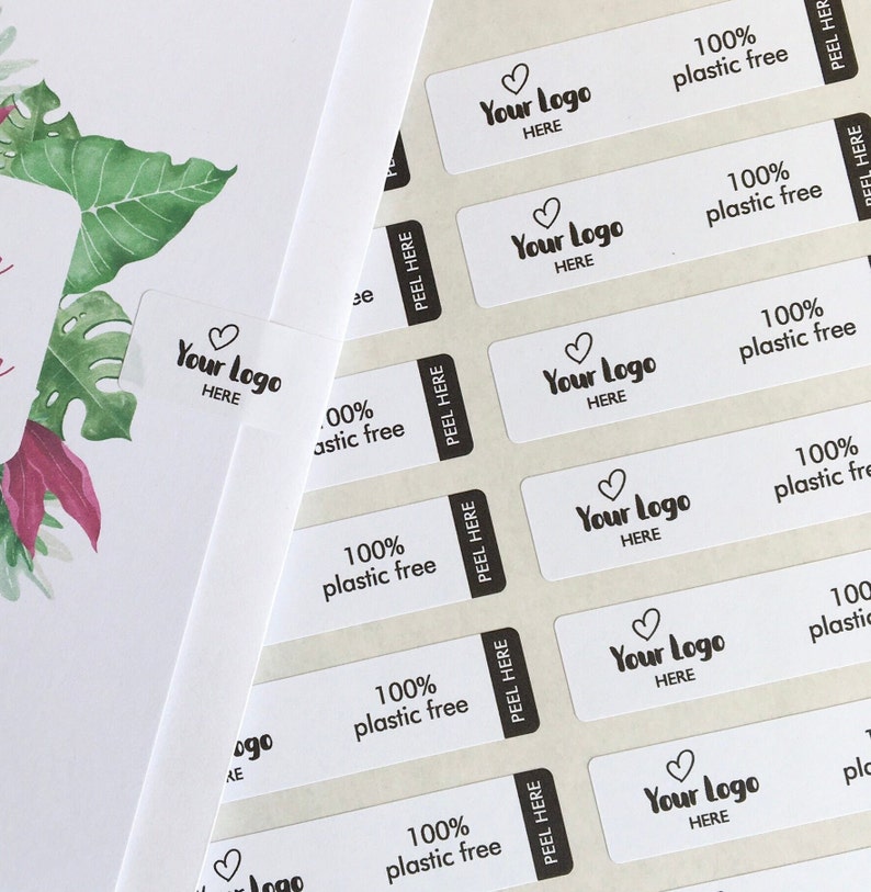 May include: White rectangular stickers with the text "Your Logo HERE" and "100% plastic free" printed in black. The stickers have a peel-off section and are arranged on a light background. A watercolor floral design is visible in the background.