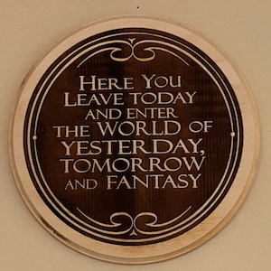 May include: A circular wooden sign with a dark brown centre and a light brown border. The sign features the words "Here You Leave Today And Enter The World Of Yesterday, Tomorrow And Fantasy" in a white, stylised font.