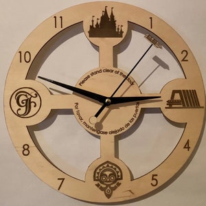 May include: A wooden clock with a unique design featuring different Disney icons. The clock face is surrounded by a circle with the numbers 1 through 12. The clock hands are black and the clock face is beige. The text "Please stand clear of the door" and "Por favor, mantengase alejado de las puertas" is printed on the clock face.