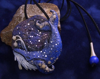 May include: A blue and white whale pendant necklace with a black cord and blue and silver accents. The whale is made of polymer clay and has a starry sky design.