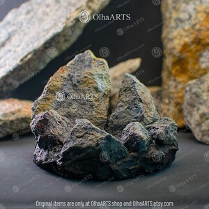 May include: A group of five gray, black, and brown rocks with a rough, textured surface. The rocks are arranged in a cluster, with the largest rock in the center. The rocks are painted with a variety of colors, including gray, black, brown, and green.