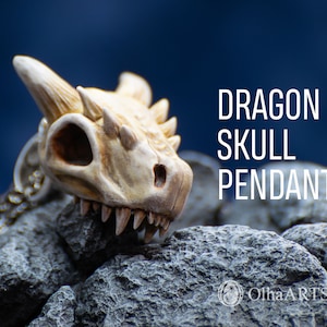 May include: A white dragon skull pendant with a silver chain. The pendant is sitting on a pile of gray rocks. The text "Dragon Skull Pendant" is written in white letters on a blue background.