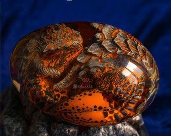 May include: A clear glass orb with a dragon encased inside. The dragon is made of a black and orange material and has a textured surface. The orb is sitting on a rocky surface.