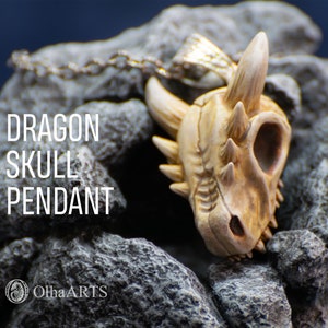 May include: A detailed dragon skull pendant made of white and beige polymer clay. The pendant is hanging from a silver chain and is resting on a bed of gray rocks. The text "DRAGON SKULL PENDANT" is visible in the image.