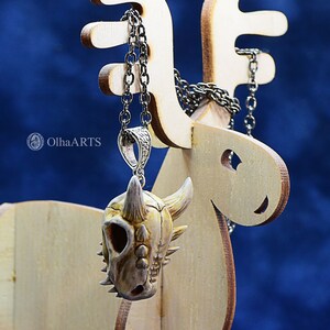 May include: A white and brown dinosaur skull pendant on a silver chain hanging from a wooden reindeer display stand.