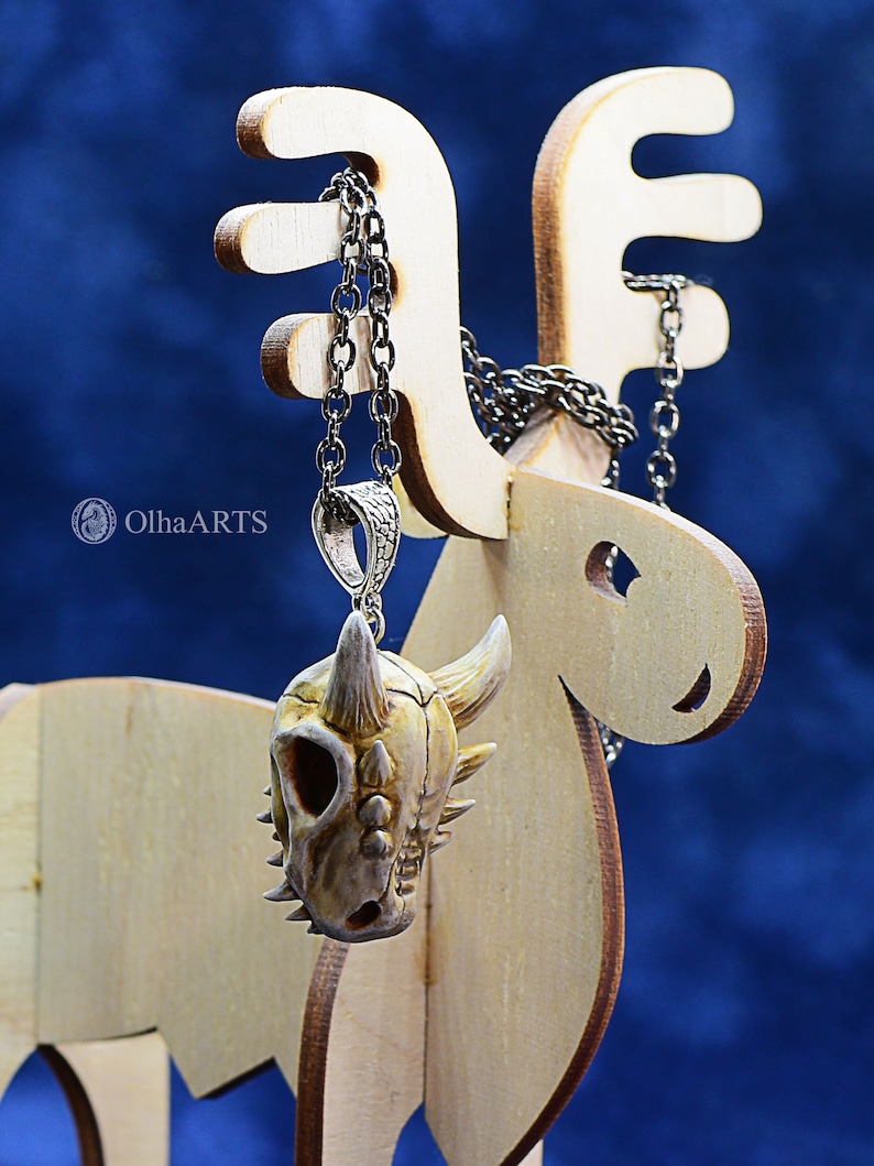 May include: A white and brown dinosaur skull pendant on a silver chain hanging from a wooden reindeer display stand.